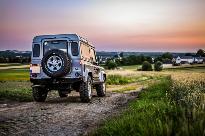 Defender op een landweg bij zonsondergang